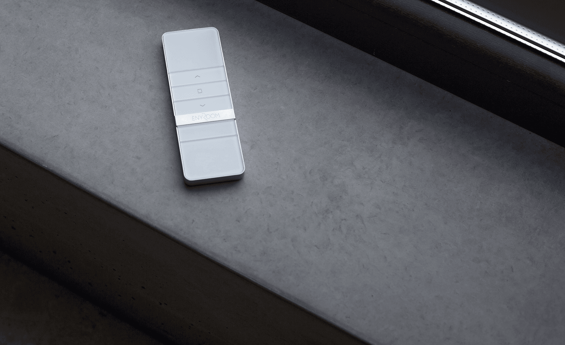 Vit fjärrkontroll för solskydd liggandes på mörk sten vid fönster