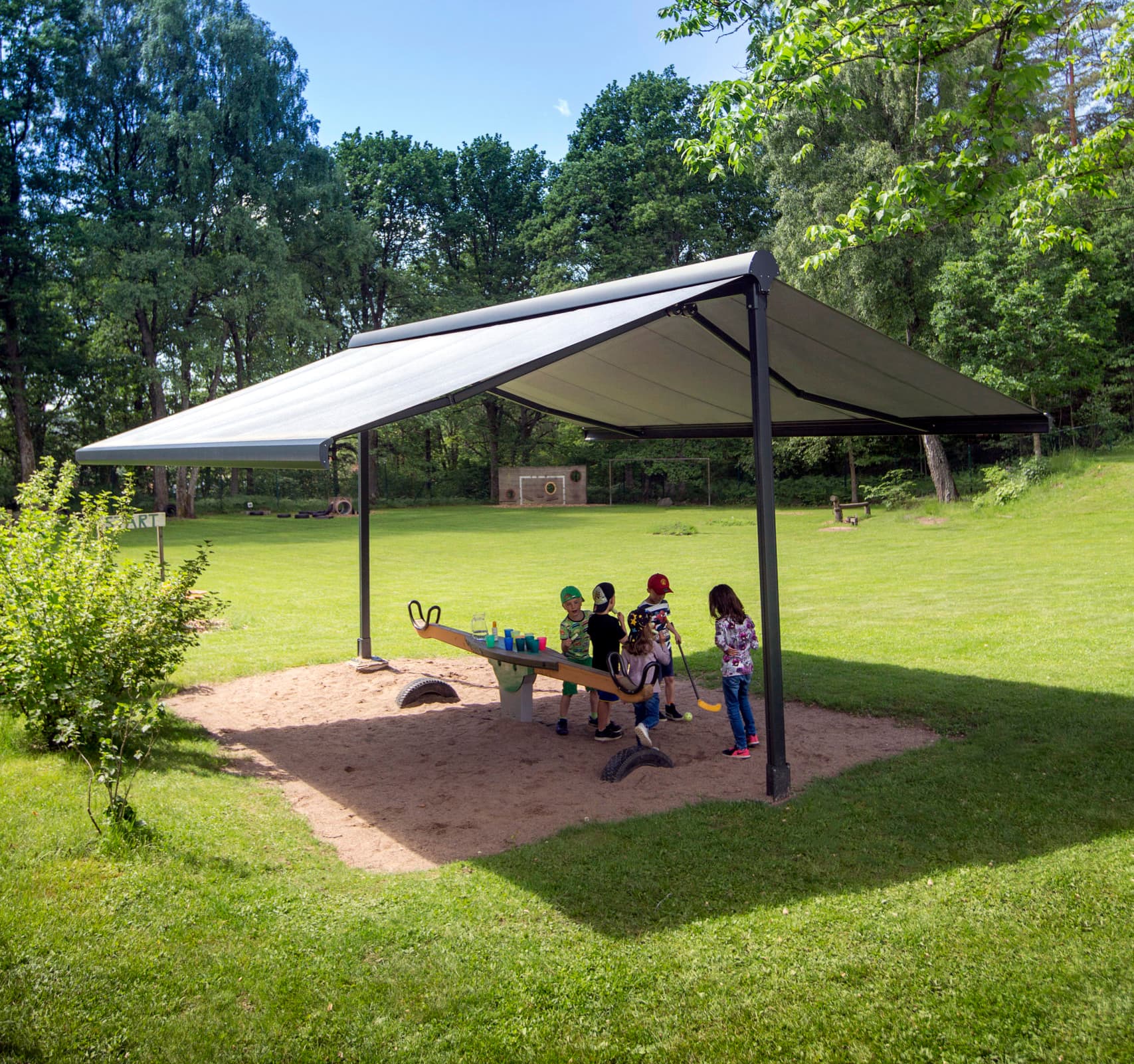 Solskydd lekplats förskola fristående markis Lekplats på öppen yta i naturen med barn förskola under fristående markis i skugga