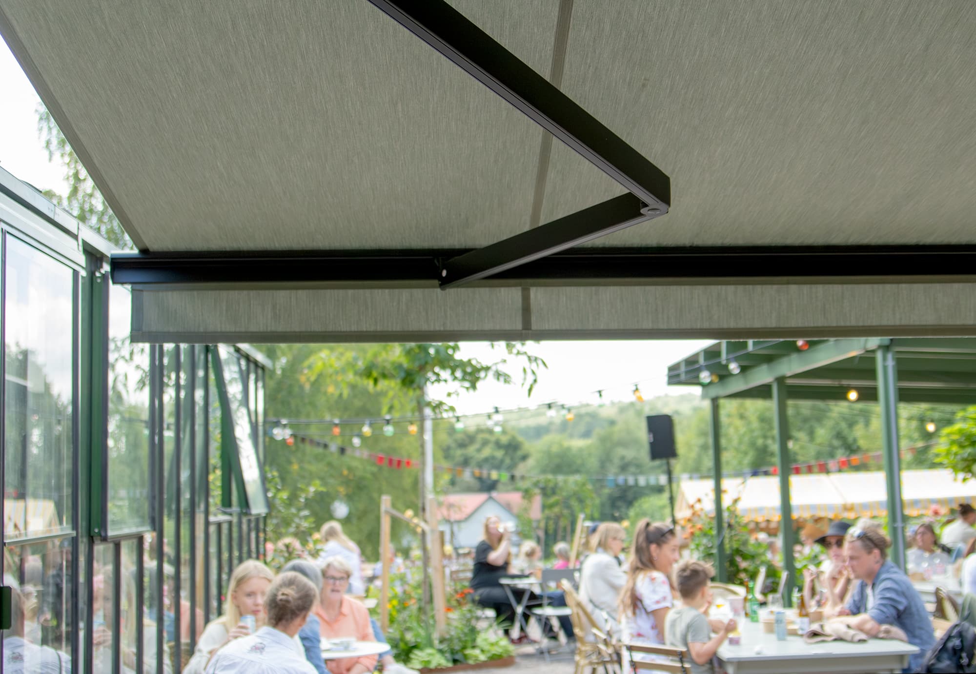 Vy under grön markis mot uteservering med människor